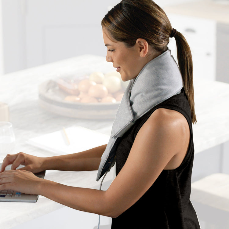 Woman using a laptop with a gray neck pillow in a bright room