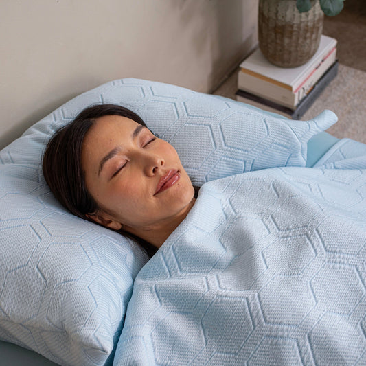 Light blue textured bedspread and pillowcases on a wooden bed in a bedroom setting.
