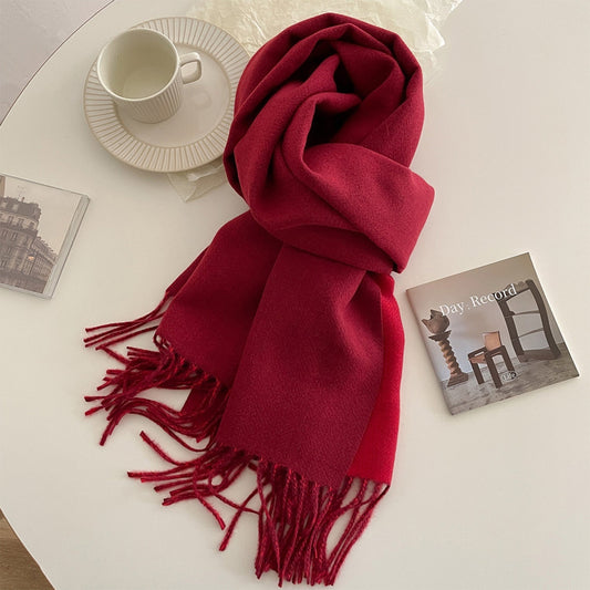 A green reversible pashmina scarf with fringe detailing, displayed on a white surface next to a beige coat and a pretzel.