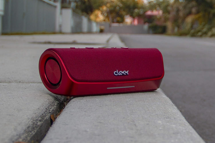 Red portable speaker with 'cleer' branding on a concrete surface outdoors.