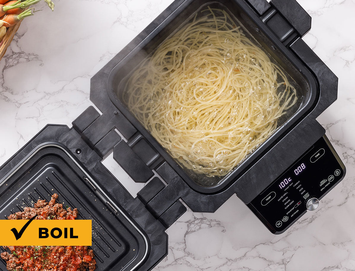 Multifunctional kitchen appliance with a pot of boiling pasta on a marble countertop.