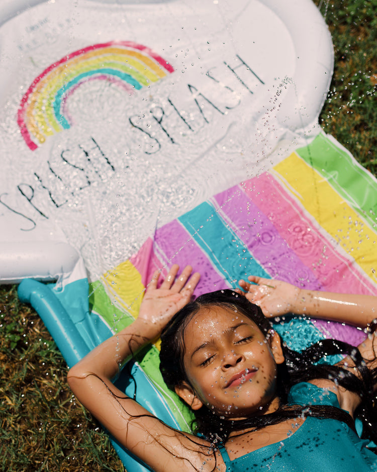 Child playing in a inflatable pool with rainbow design and 'Splash Splash' text.