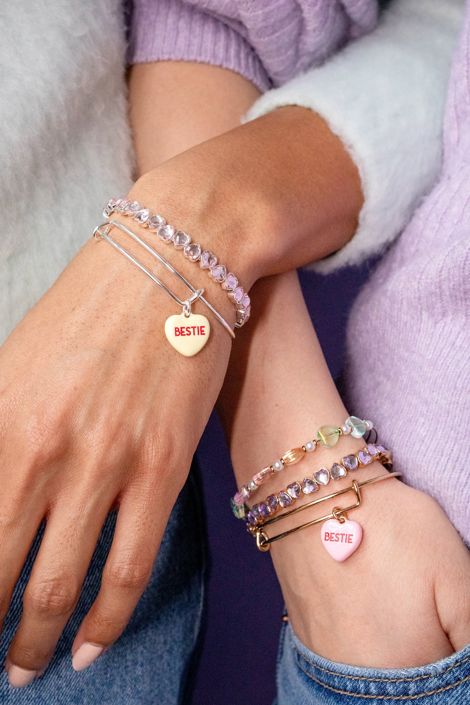 Close-up of hands wearing multiple bracelets with heart-shaped name tags.