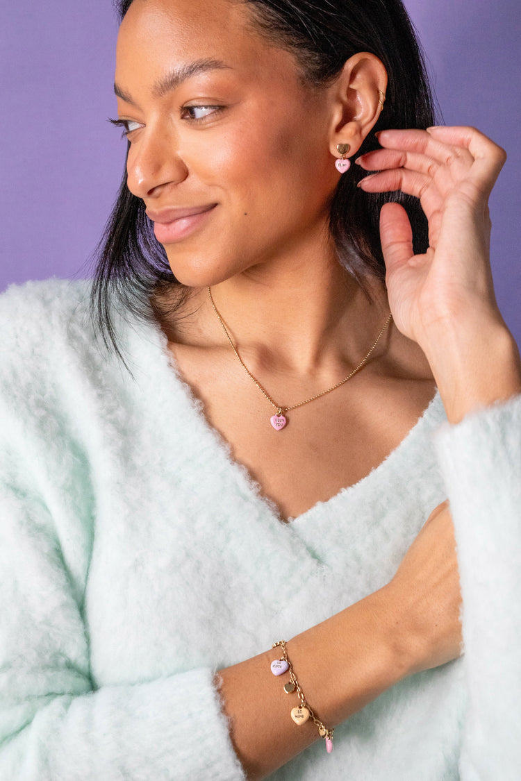 Woman wearing a gold bracelet with heart charms against a purple background
