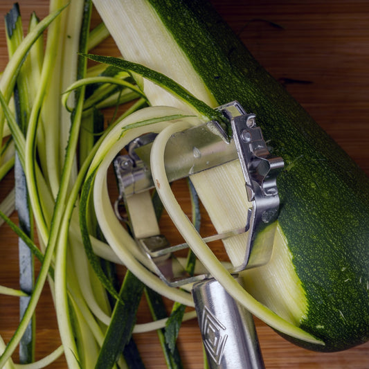 Set of kitchen tools including a peeler, mandoline, and other cutting tools with sliced vegetables on a white background.