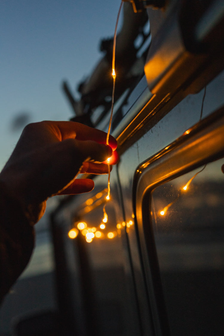 Hand holding a string of lights against a vehicle at sunset