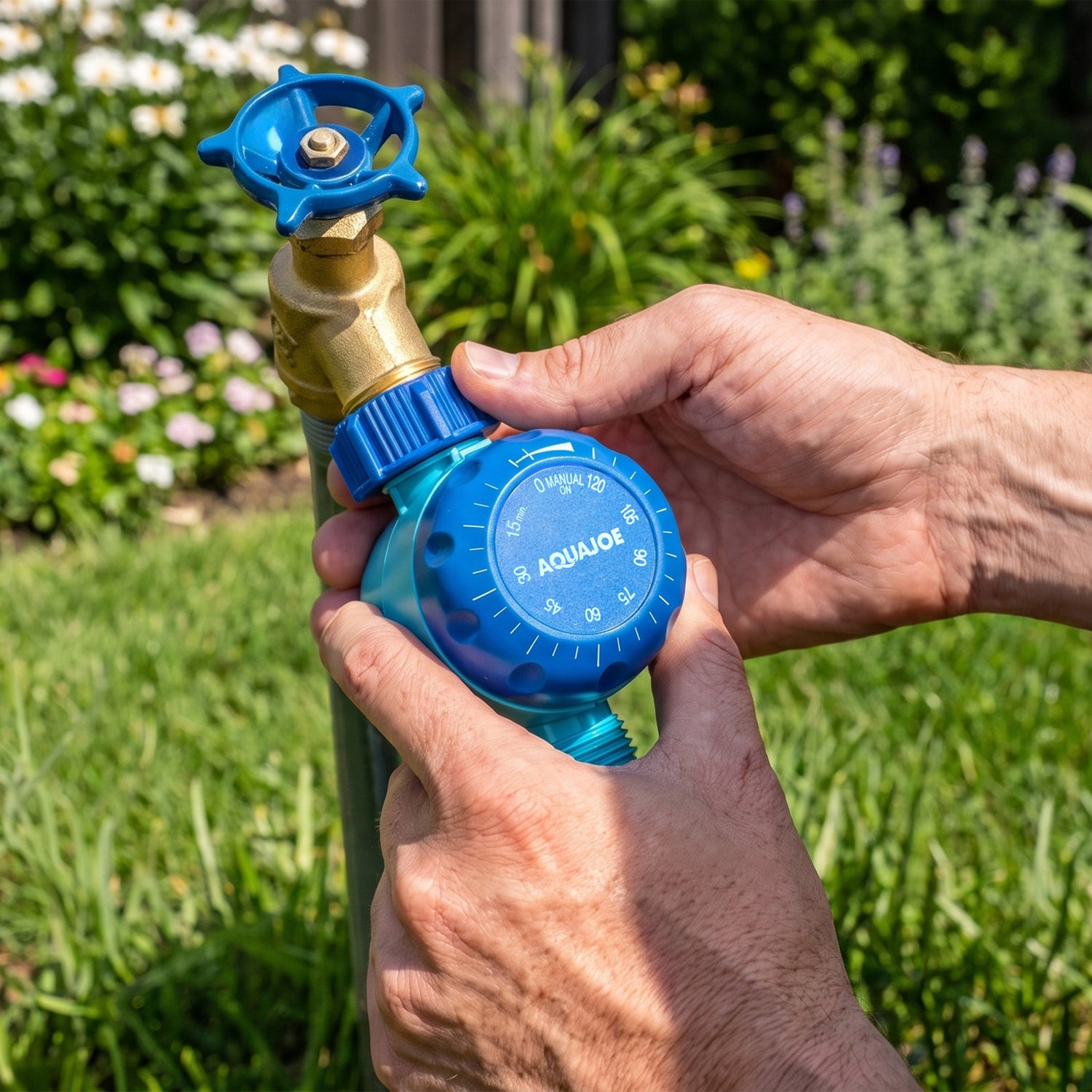 A close-up of a person's hands adjusting a blue and teal Aquajoe self-watering garden hose valve outdoors in a grassy garden setting.