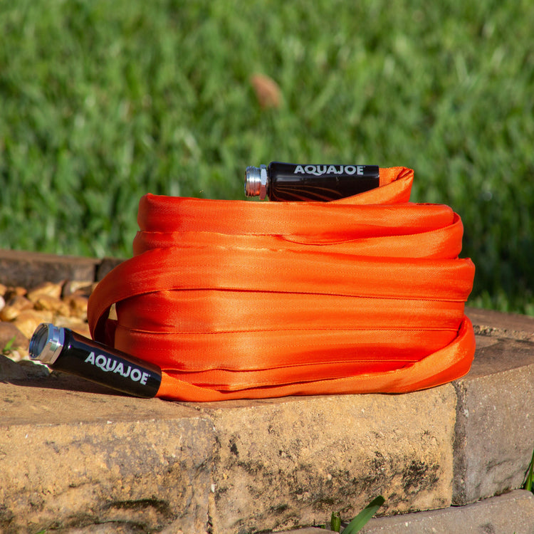 Orange hose with Aquajoe branding on a stone ledge with grass in the background