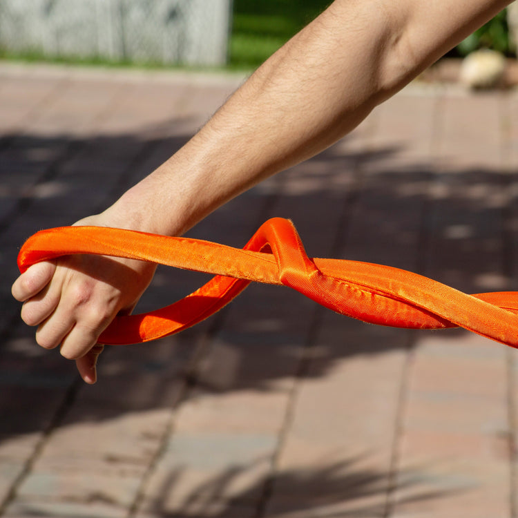 Person holding an orange resistance band outdoors on a sunny day.