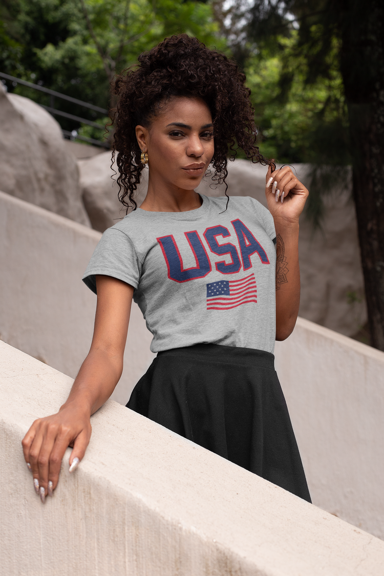 Woman wearing a gray t-shirt with 'USA' and an American flag design, standing outdoors.