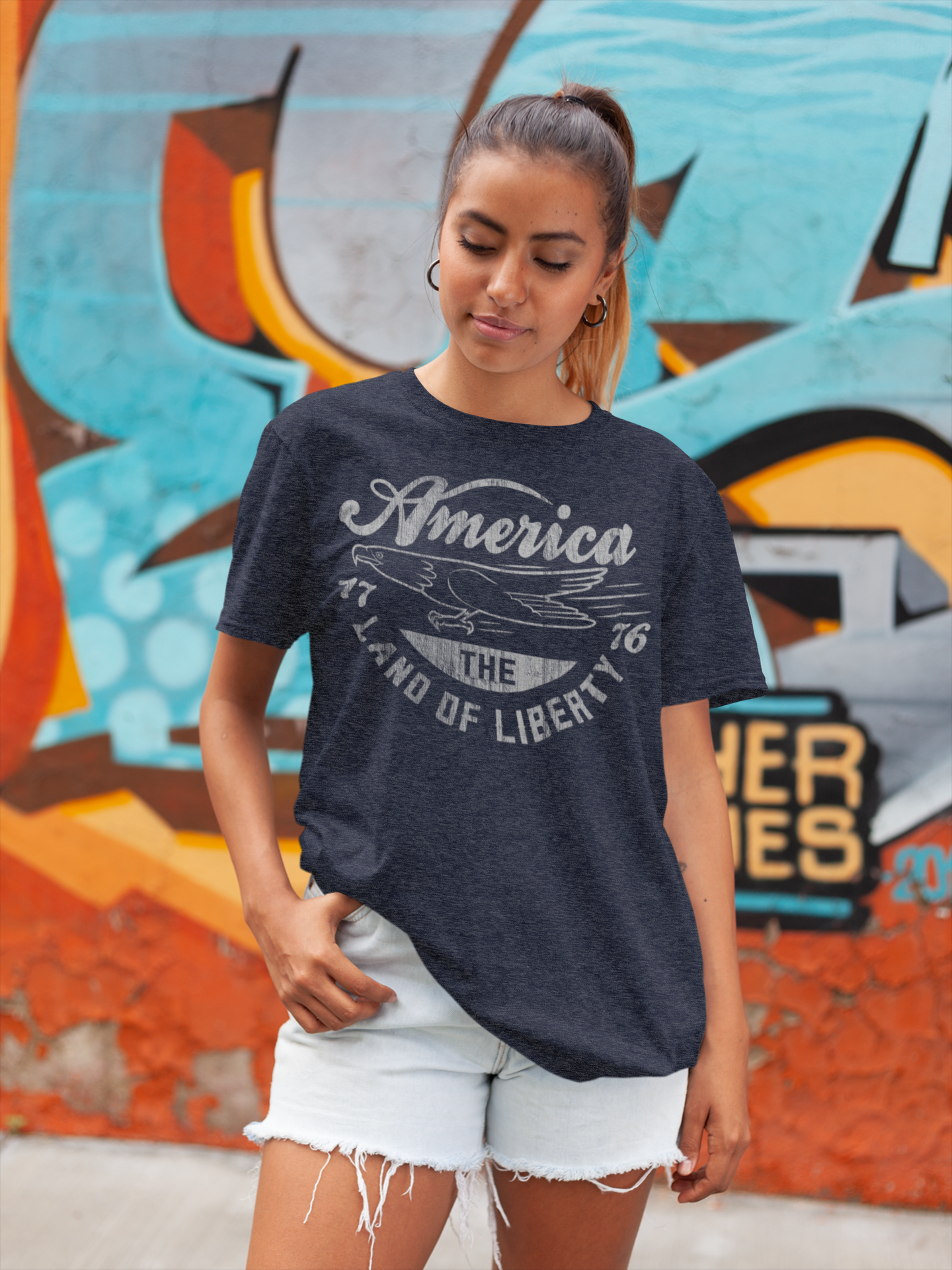 Woman wearing a navy blue t-shirt with 'America, Land of Liberty' text in front of colorful graffiti.