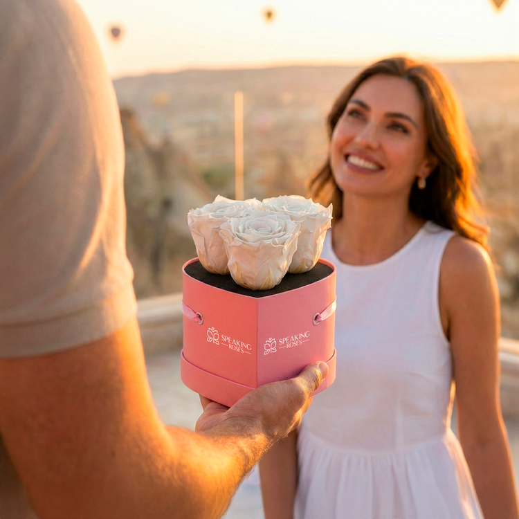 Person holding a pink box with a white rose against a blurred outdoor background