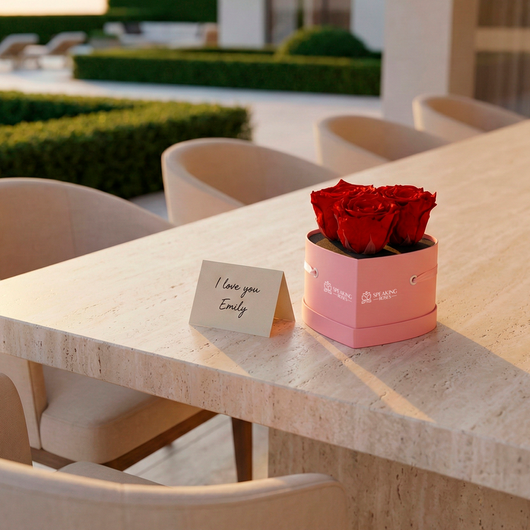 Pink box with red roses and 'I love you Emily' card on a table outdoors.