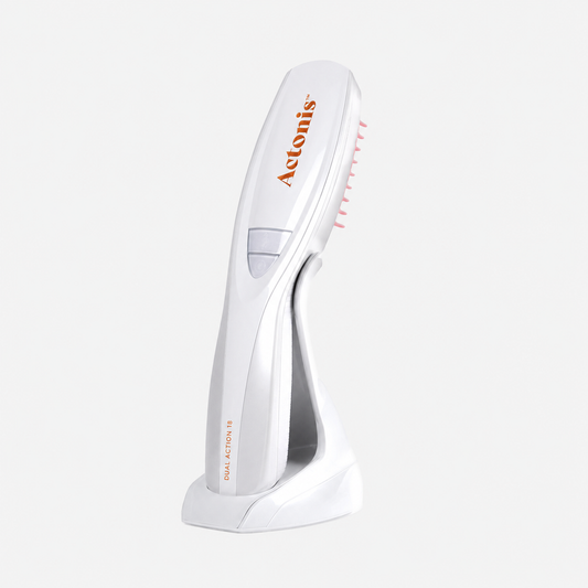 Actonis hair loss reduction device in white with orange branding, standing on its charging base against a light gray background.