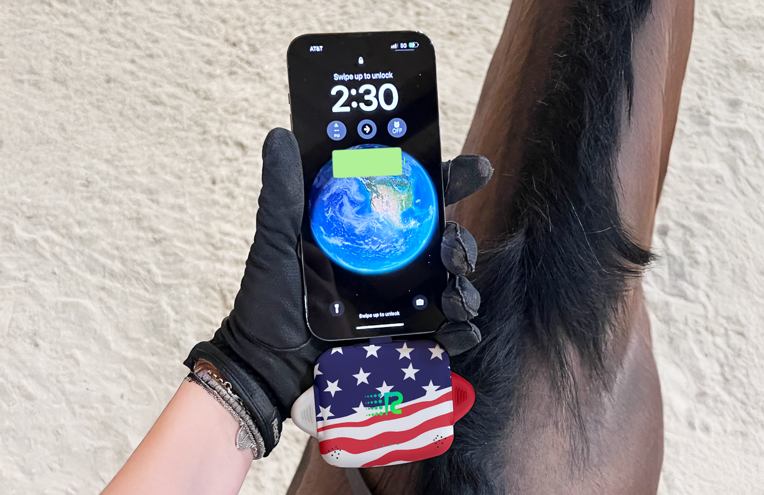 Hand wearing a black glove holding a smartphone with a horse's ear in the background