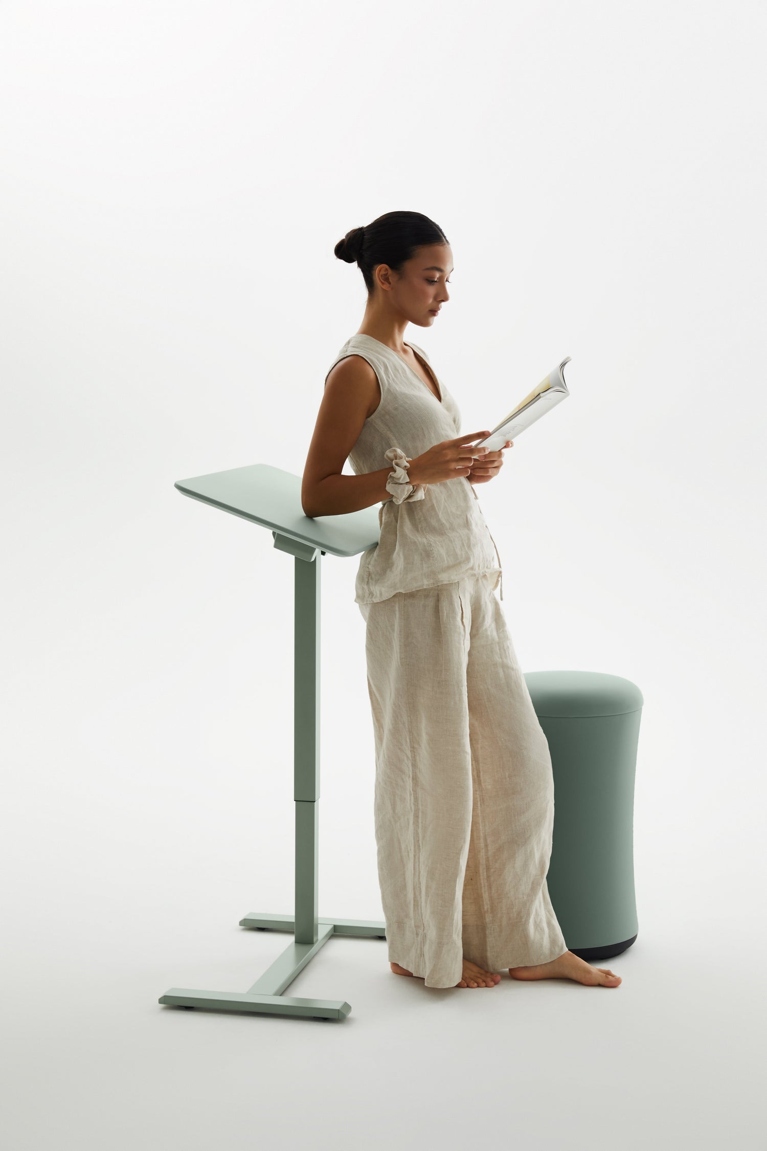 Woman in a white outfit standing next to a standing desk on a white background