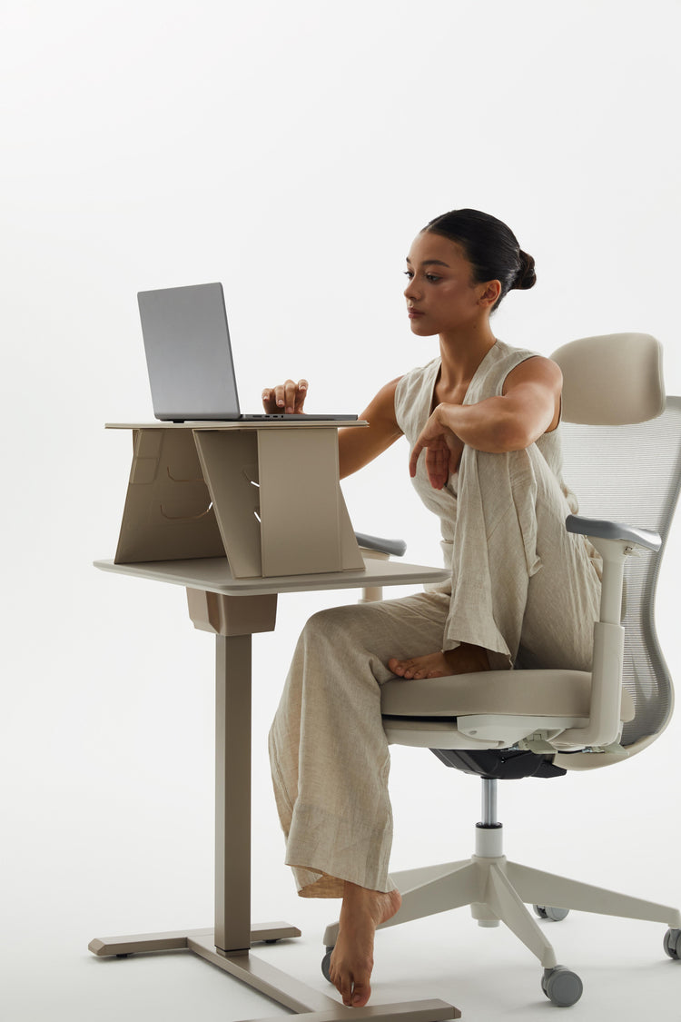 Woman using a laptop on a height-adjustable desk with a white background