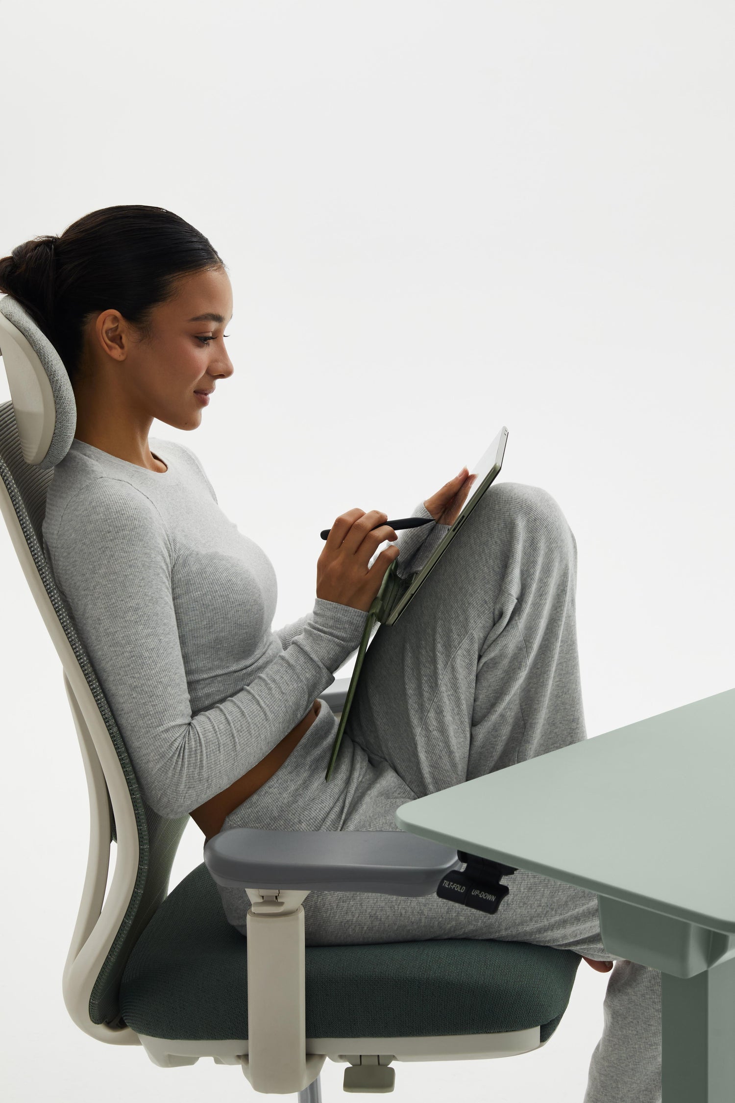 Woman sitting on a modern office chair using a tablet at a desk.