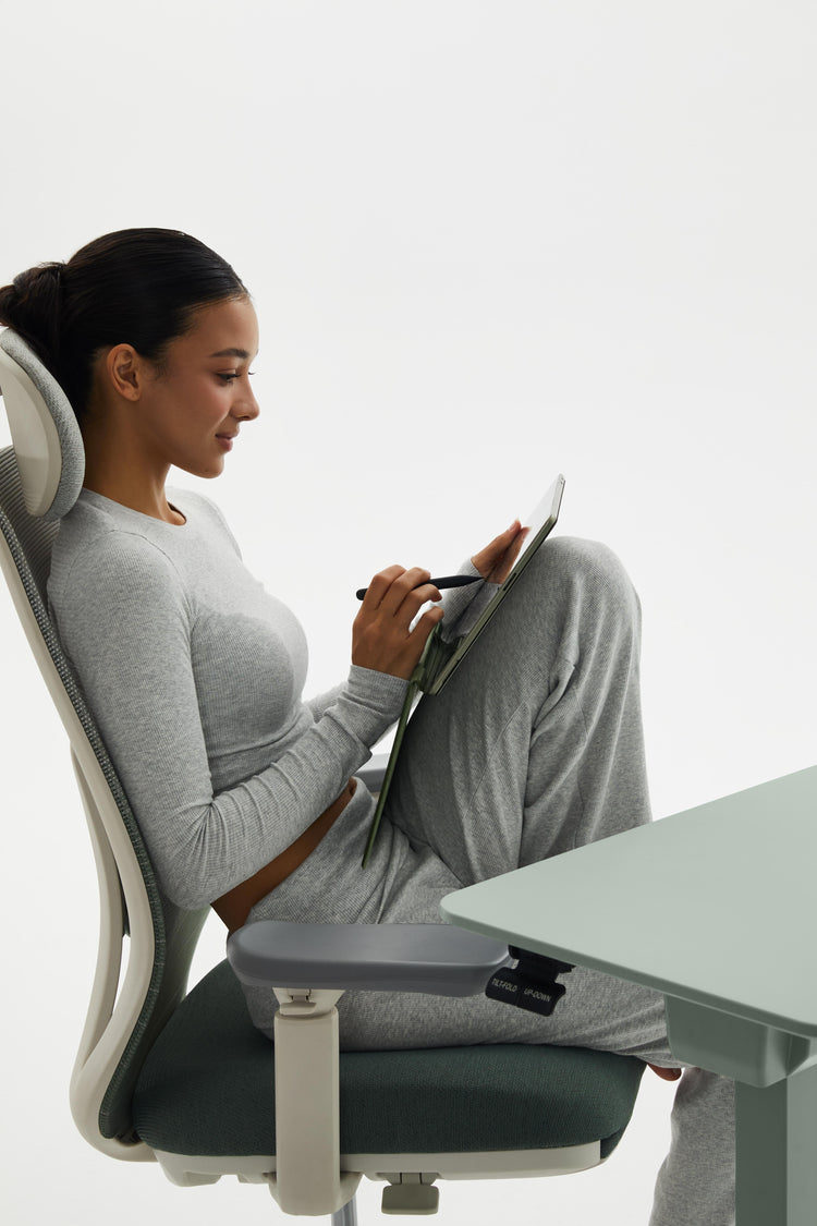 Woman sitting on a modern office chair using a tablet at a desk.