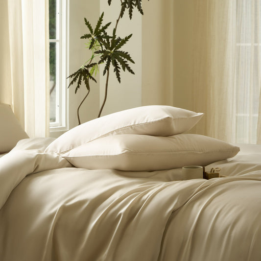 Neatly made bed with beige bedding in a bright room with large windows.