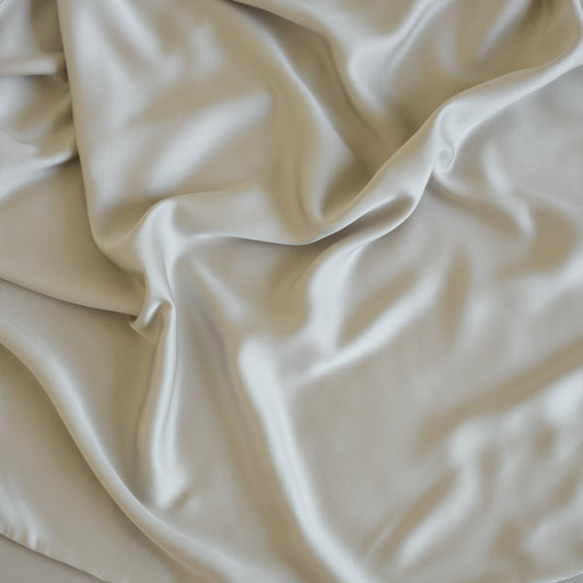 Neatly made bed with beige bedding in a bright room with large windows.