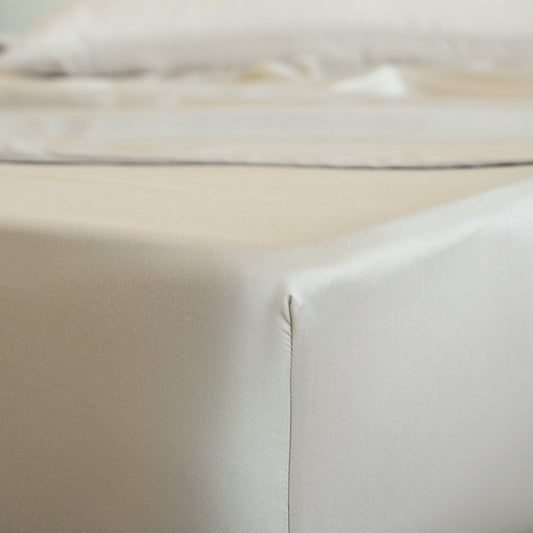 Neatly made bed with beige bedding in a bright room with large windows.