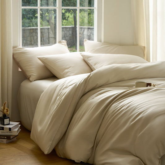 Neatly made bed with beige bedding in a bright room with large windows.
