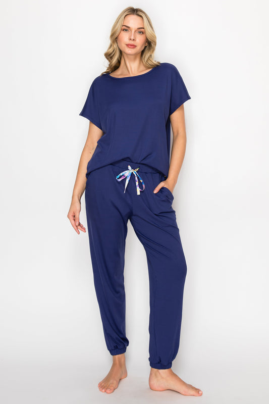 Woman wearing navy blue pajama set in a bedroom and bathroom setting.