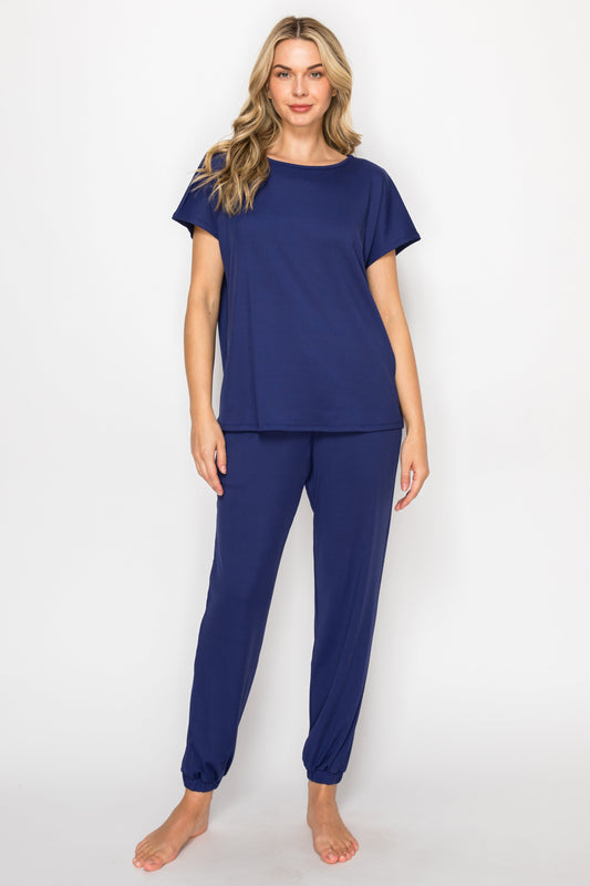 Woman wearing navy blue pajama set in a bedroom and bathroom setting.