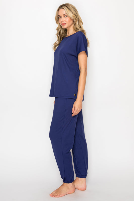 Woman wearing navy blue pajama set in a bedroom and bathroom setting.