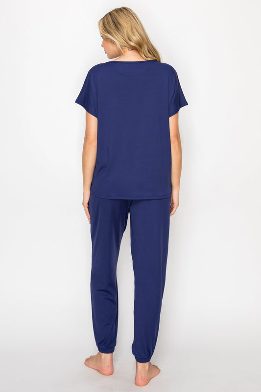 Woman wearing navy blue pajama set in a bedroom and bathroom setting.