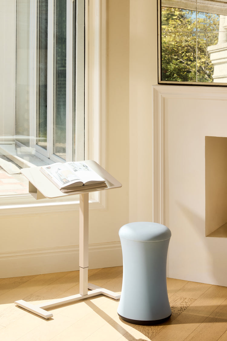 Light blue stool in a room with a window and a standing desk.