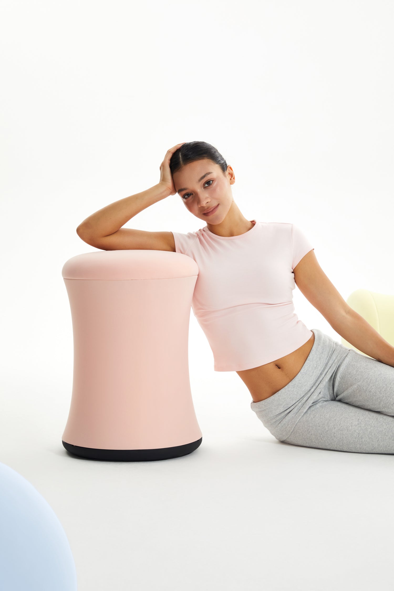 Woman sitting on a pink stool against a white background