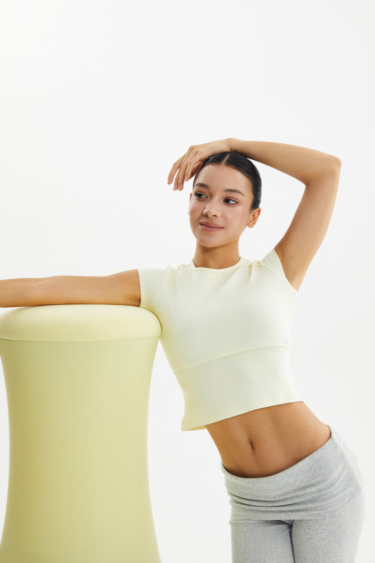 Woman in a light yellow top and gray pants posing against a white background