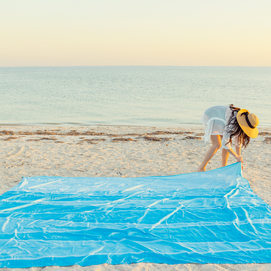 Woman spreading a blue towel on a sandy beach with ocean in the background