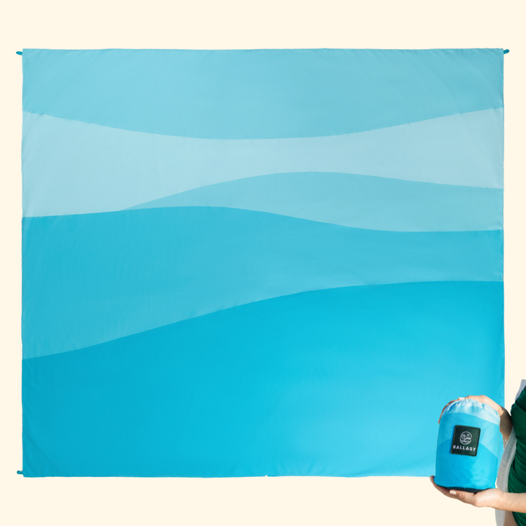 Blue beach towel with a person holding a blue container on a beige background