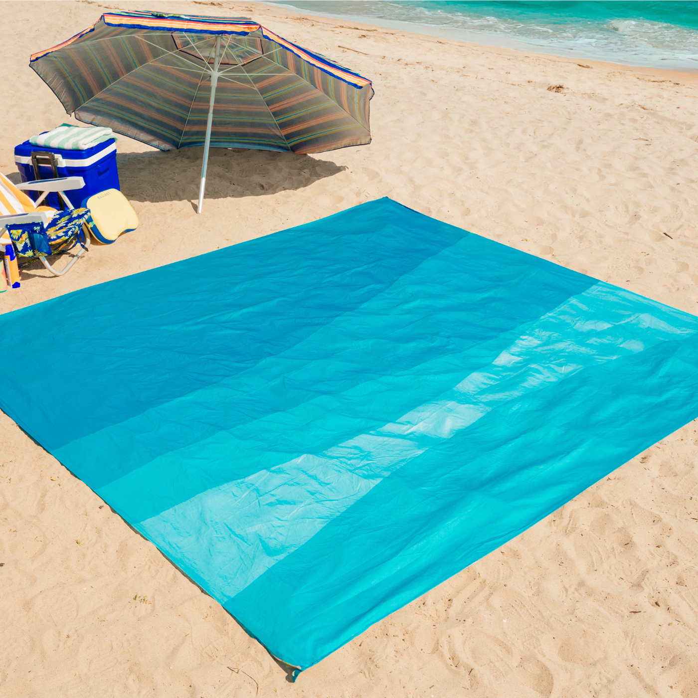 Blue sand-resistant mat on a sandy beach with an umbrella and cooler in the background.