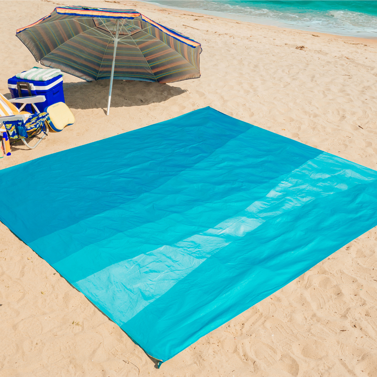 Blue sand-resistant mat on a sandy beach with an umbrella and cooler in the background.