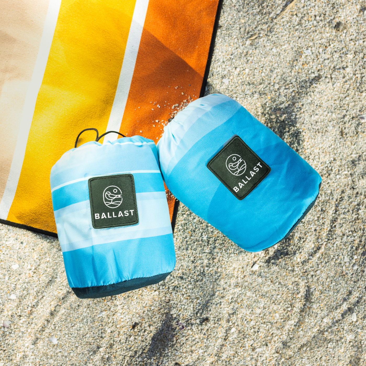 Two blue beach bags with 'Ballast' branding on a sandy surface.