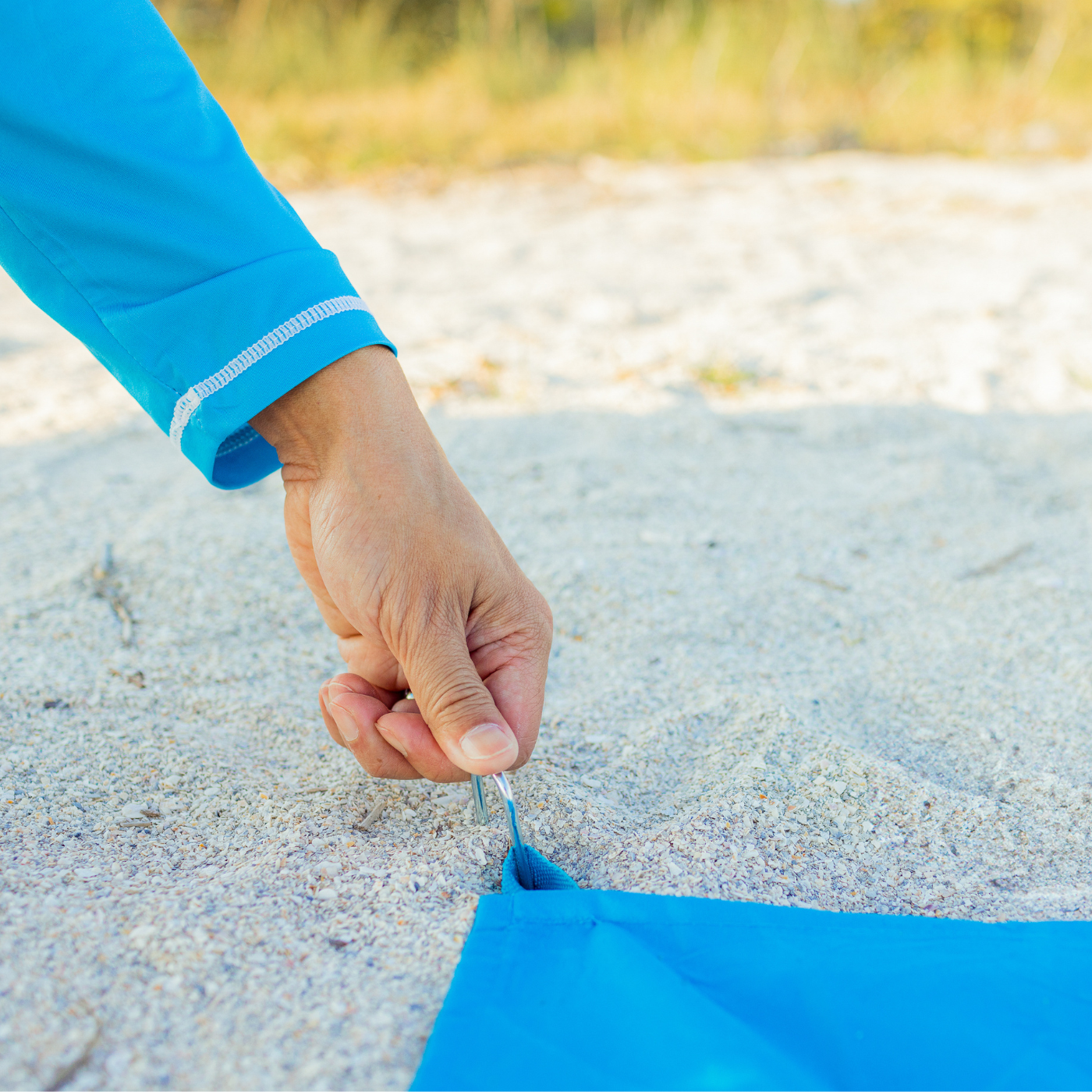 Hand setting up a blue tent on sandy ground