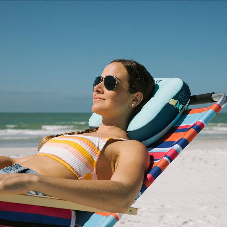 Woman relaxing on a colorful beach chair with a pillow, ocean in the background