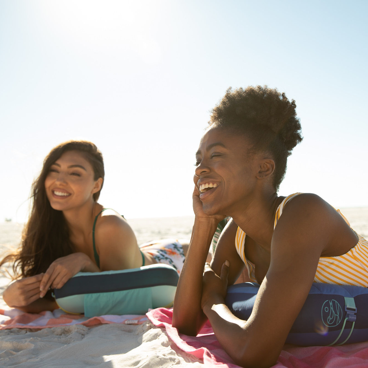Two women sitting on a beach blanket, laughing and enjoying each other's company.