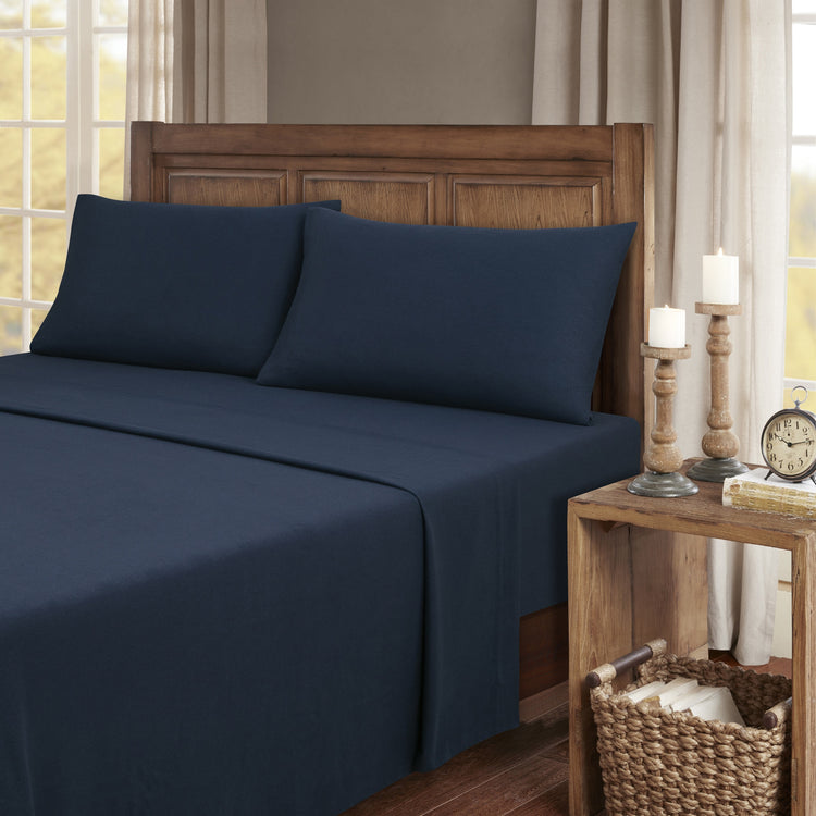 Navy blue bed sheets on a neatly made bed with wooden headboard and nightstand.