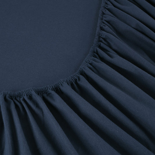 Navy blue bed sheets on a neatly made bed with wooden headboard and nightstand.
