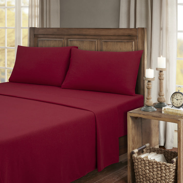 Red bed sheets on a wooden bed with a wooden nightstand and decor items.