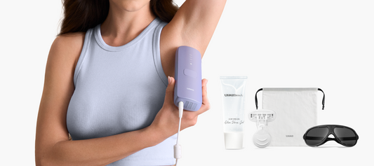 Woman using a purple electronic device on her arm with a bottle, pouch, and sunglasses in the foreground.