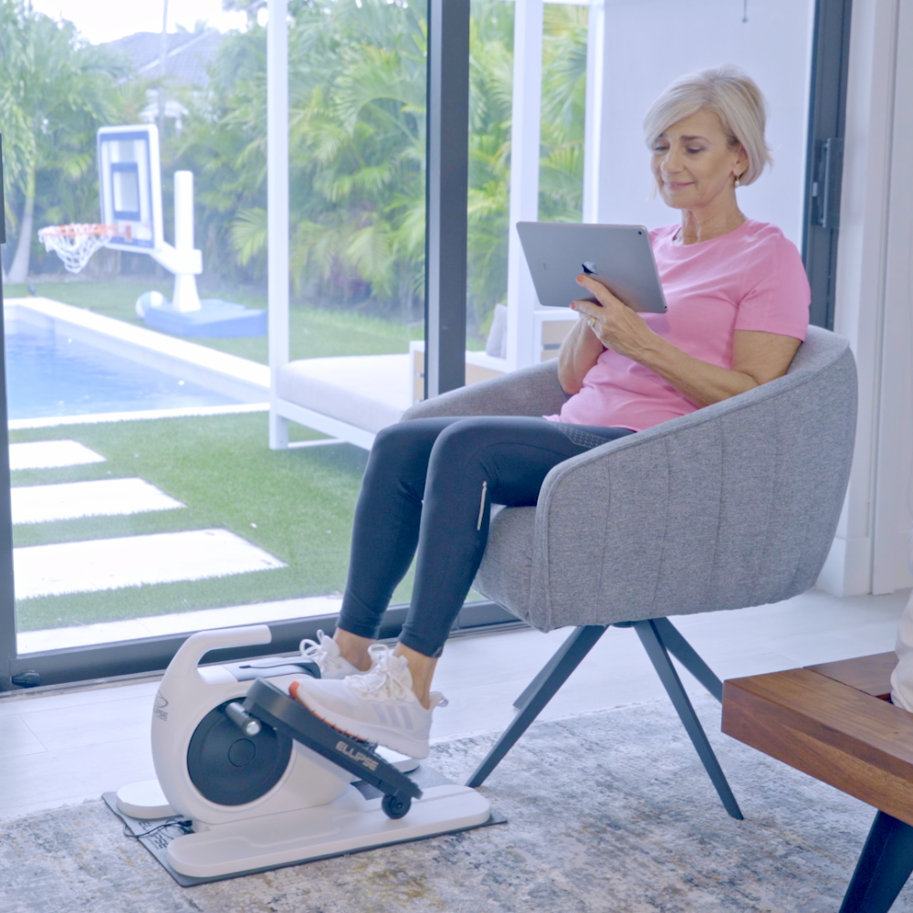 Woman using a home exercise bike and tablet in a modern living room.