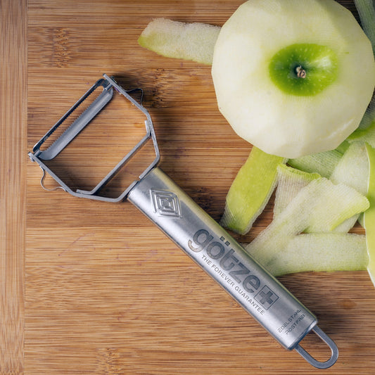 Set of kitchen tools including a peeler, mandoline, and other cutting tools with sliced vegetables on a white background.