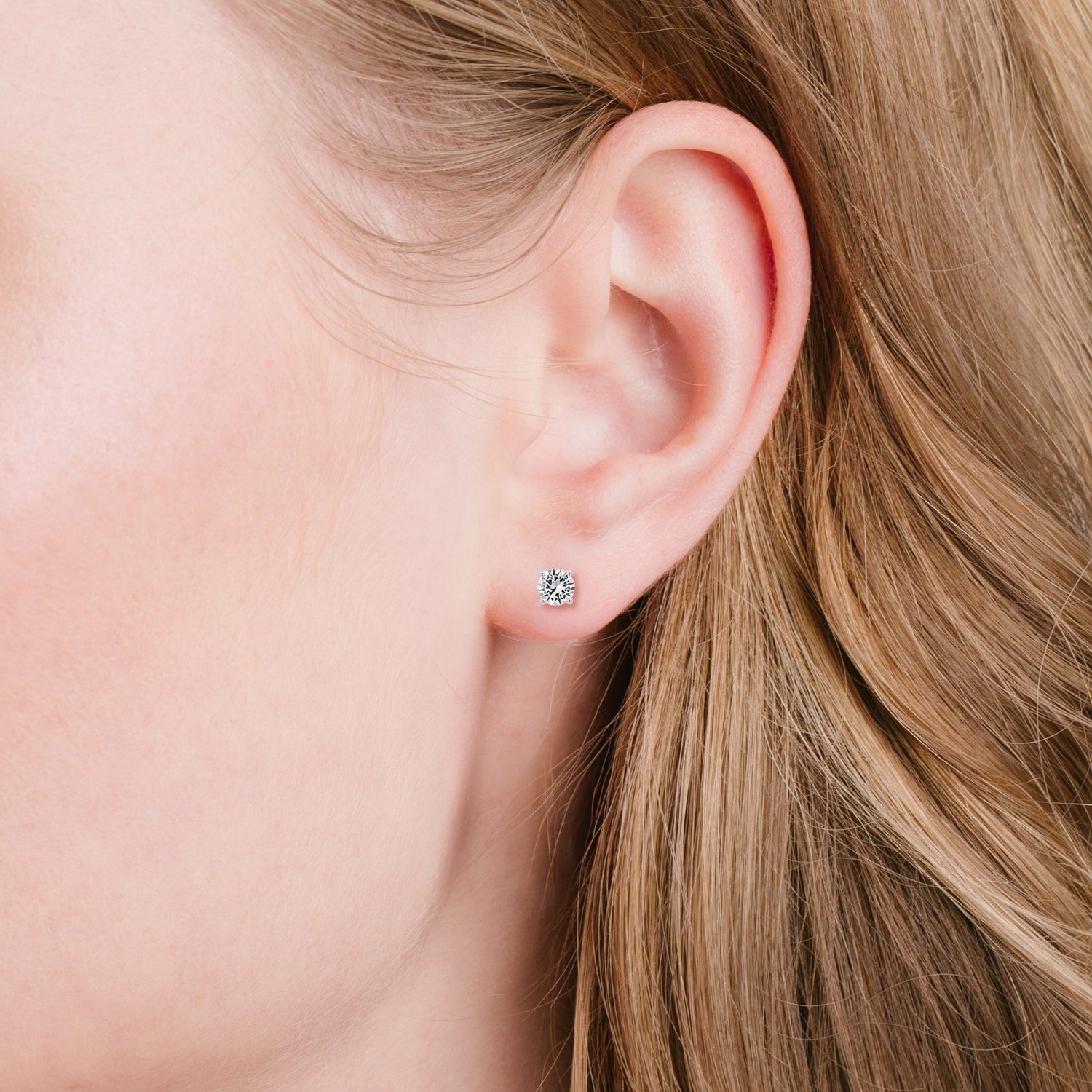 Close-up of an ear wearing a silver earring with a clear gemstone, with blonde hair partially visible.