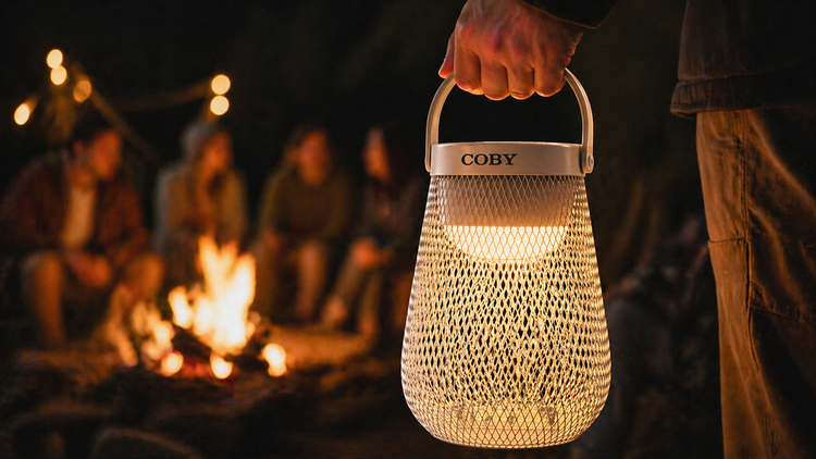 Coby lantern held by a person with a campfire and people in the background